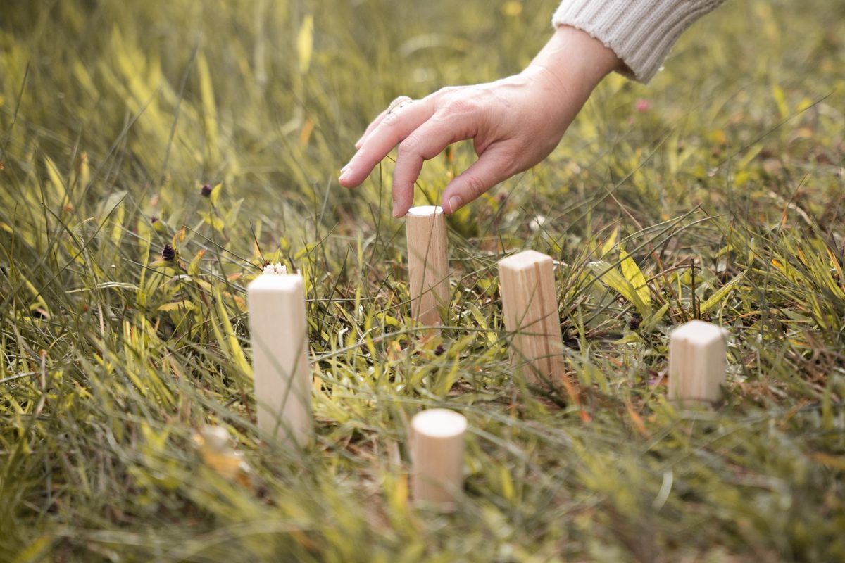 Eine Hand stellt Holzfiguren für eine systemische Aufstellung in die Wiese